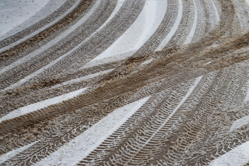 Multiple vehicle tire tracks forming intersecting patterns on a slushy and dirty snow-covered road during winter weather conditions.