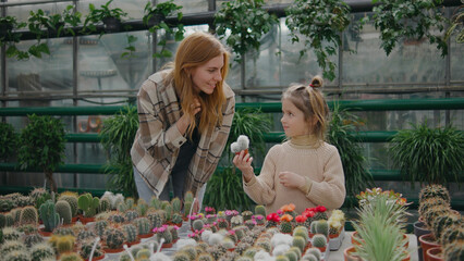 Mother and daughter share a moment in a greenhouse filled with various colorful cacti and plants while exploring their options for home decor