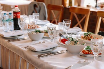 View of a beautifully set dining table with white tablecloths, bowls of salad, plates, crystal glasses, and silverware, ready for a formal reception
