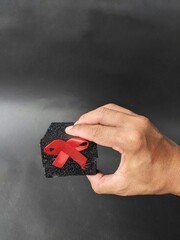 Hand holding a gift box wrapped with red ribbon on a dark background. Black Friday