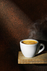Ray of light falls on small white cup espresso standing on board against brown background