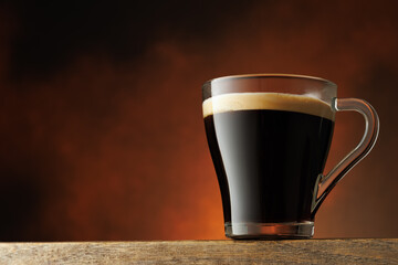 Transparent cup of hot coffee stands on the table on brown background