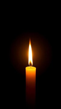 Solitary yellow candle brightly burning with glowing flame casting light in the darkness creating a warm and hopeful mood.