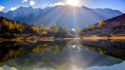 Mountain valley in autumn with a calm lake. The bright yellow of the leaves contrasts with the dark water and the deep blue of the far peaks and sky.