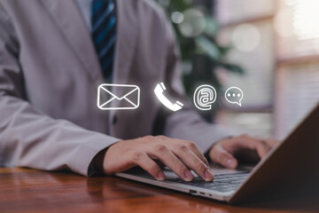 A businessman typing on a laptop with floating contact icons, symbolizing online communication,...