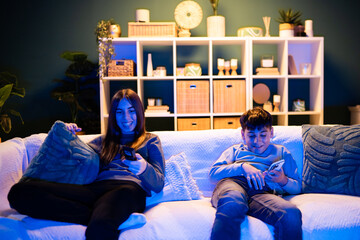 Young siblings using smartphones on couch at home