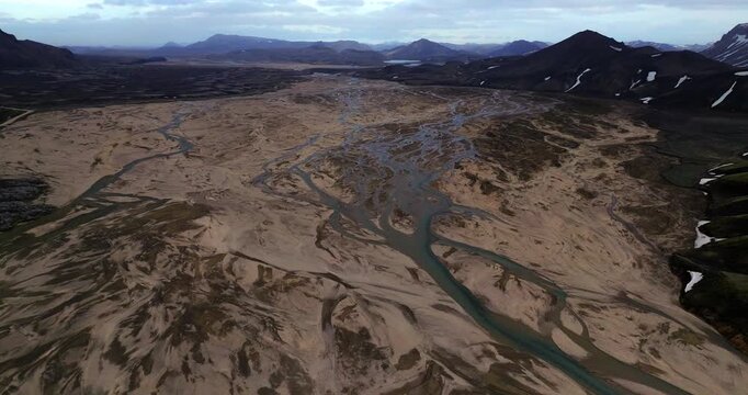 The drone glides over Landmannalaugar&rsquo;s volcanic terrain, revealing sweeping vistas of layered mountain slopes, river channels, and shimmering mineral tones that define this Icelandic highland paradis