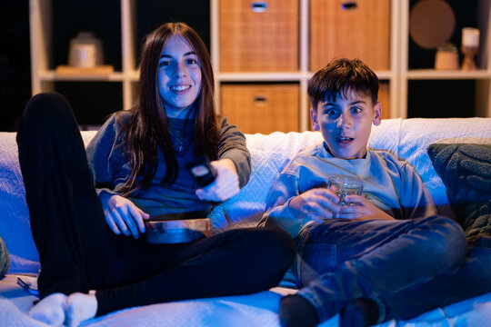 Teen siblings watching tv at night with remote - Powered by Adobe