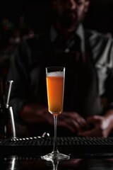 Obraz premium Cóctel espumoso tipo Bellini en copa flauta con espuma, barra de coctelería elegante, Mimosa dorada servida en copa alta en bar oscuro, mixología de autor