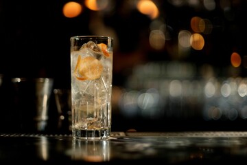 Fototapeta premium Cóctel elegante en vaso alto con twist de piel de naranja, Bebida de autor en barra de bar con iluminación cálida, Vaso de cristal tallado con bebida espirituosa y atmósfera nocturna