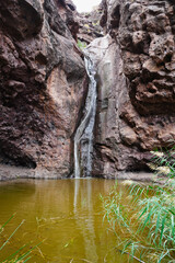 A small waterfall flowing down volcanic rock walls into a still pool, set in the rugged natural surroundings of Charco Azul in Agaete on the island of Gran Canaria