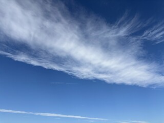 Vibrant blue sky with wispy cirrus clouds and a faint contrail stretching across, creating a peaceful and spacious background for nature or travel themes.