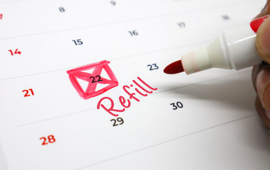 Hand marking a calendar with a bright red pen to schedule a crucial Refill date, emphasizing timely health management and appointment organization