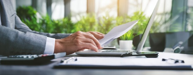 The businessman reviewing documents at a sunlit modern office desk with laptop