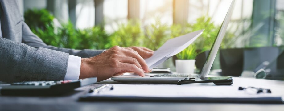The businessman reviewing documents at a sunlit modern office desk with laptop