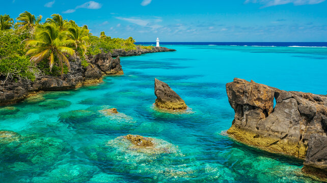 Tropical turquoise lagoon with rocky coastline, lush green vegetation, and distant lighthouse