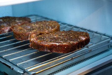 Raw ribeye steak dry brine with salt, bell pepper, and aromatic herbs rub, placed inside a fridge on a stainless steel tray