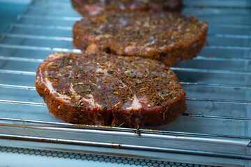 Raw ribeye steak dry brine with salt, bell pepper, and aromatic herbs rub, placed inside a fridge on a stainless steel tray