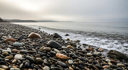 Pebbles line a misty shoreline as gentle waves lap the shore.