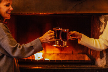 The women toast and clink glasses with mulled wine. Girls in sweaters celebrate a festive meeting and drink a spicy hot Christmas drink at a house party.