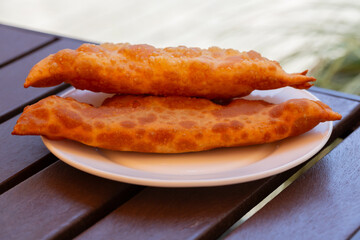 Hearty lunch: Chebureks with meat on a white plate on a wooden table. Big chebureks for dinner. Meat pies. Close-up.