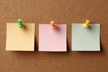 Three colorful blank square notes held by pushpins on a textured brown cork board background