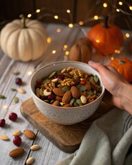 Hand Holding Bowl of Trail Mix with Pumpkins and String Lights
