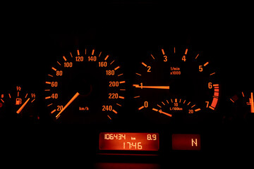 Close up of a speedometer in a car, illuminated with orange light. After edits.