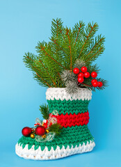 Beautiful knitted Christmas slipper filled with fir branches on a blue background