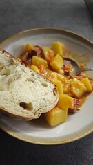 Stew with potatoes, carrots and sausage served with a slice of fresh bread on a ceramic plate