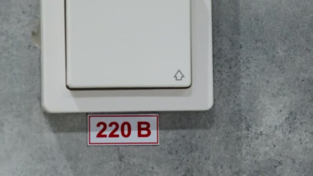Light switch attached to wall allows control of illumination. Button designed for turning light on and off installed near voltage indication