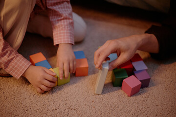 Child and Adult sitting on carpet arranging colorful wooden blocks together, hands visible...