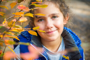 In the park in autumn, a little girl looks through the leaves.