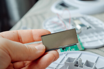 Close-up of a hand holding an LCD display module from a disassembled electronic device. Useful for tech repair, DIY electronics, hardware maintenance, and product teardown concepts.