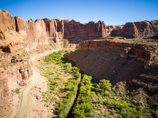 Dirt road leading up a canyon in Utah with a river bright day