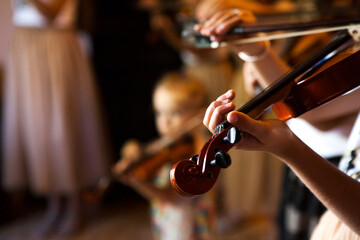 A lively youth violin ensemble rehearses on stage, young musicians in coordinated outfits bowing and playing in harmony under soft stage lights