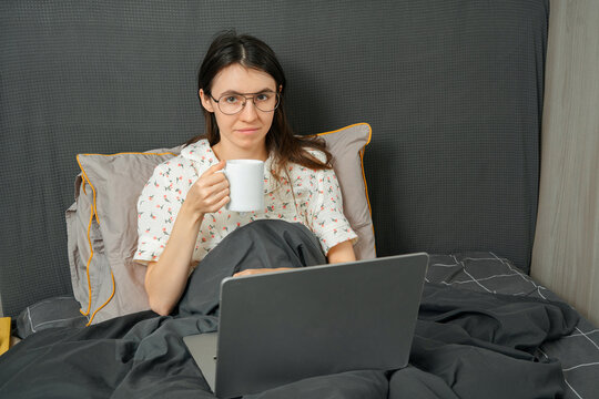 Woman working on laptop in bed with coffee mug