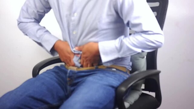 Stomach ache, stomach cramps and a man sitting in a chair at work due to indigestion, diarrhea, or food poisoning.A man has a stomach ache due to constipation, IBS, or abdominal muscle tension at home