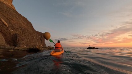 Kayaker ocean sunset paddling along rocky coast at golden hour, peaceful sea adventure at dawn