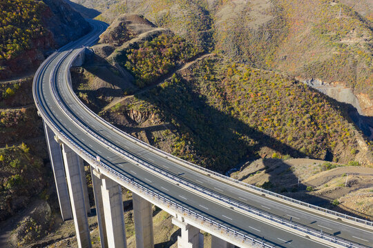 Aerial close-up of the A1 motorway bridge curving through the rugged autumn hills of Kolsh in Kukës County, Northern Albania.