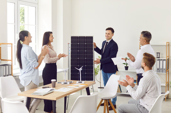 Smiling confident project manager presents renewable energy sources solar panel in a business people meeting for team in an office. Company employees applauding to colleague after presentation.