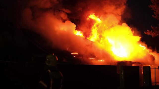 A house fire breaks out at night, producing large flames and heavy smoke that spreads in the residential area, alarming nearby residents.