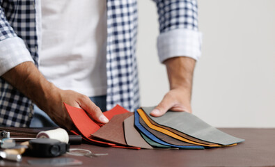 Male tailor choosing leather samples for crafting in workshop