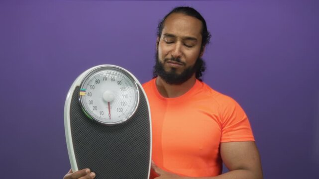 Man holding a bathroom scale and pressing hand to forehead in purple studio; frustration weight concern.