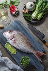 Overhead shot of a raw fish on a blue cutting board with props: Knife, vegetables, white wine,...