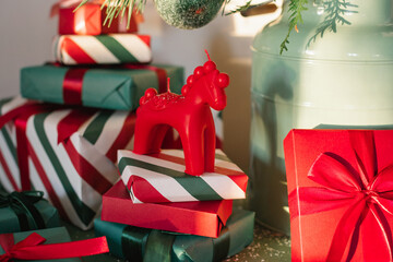 A Christmas horse ornament on top of a stack of wrapped presents placed under a decorated fir branch
