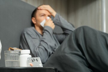 Sick man in bed with tissues and medicine on bedside table