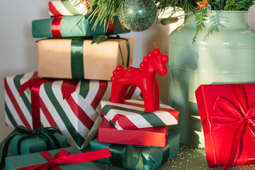 A Christmas horse ornament on top of a stack of wrapped presents placed under a decorated fir branch