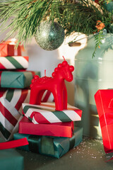 A Christmas horse ornament on top of a stack of wrapped presents placed under a decorated fir branch