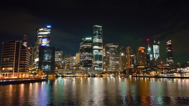 Sydney city skyline at night, modern skyscrapers with illuminated windows and vibrant urban landscape, reflecting colorful lights on tranquil harbor waters during the evening. Drone flight footage